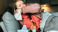 Woman sitting on a sofa coughing, illustrative of flu symptoms (Getty Images)