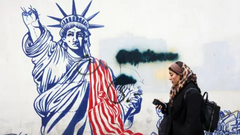 An Iranian woman walks past an anti-U.S. mural in Tehran depicting a damaged Statue of Liberty. EPA/Shutterstock.