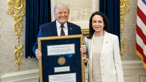 Maria Corina Machado stands beside Donald Trump as he holds a Nobel Peace Prize medal during a White House meeting (Reuters)