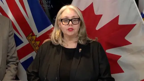 British Columbia Public Safety Minister Nina Krieger speaks at a press conference in front of Canadian flags