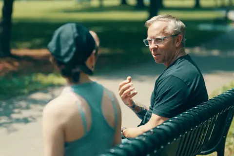 Lucy (a pseudonym), now an adult, speaks with investigator Greg Squire on a park bench