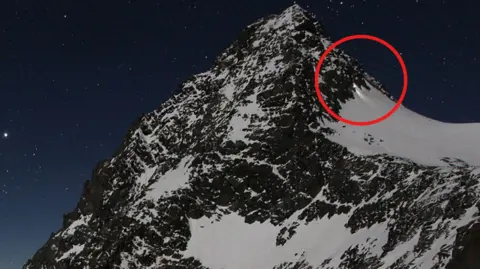 Nighttime webcam view of Grossglockner with a red circle highlighting a climber's torch near the peak.