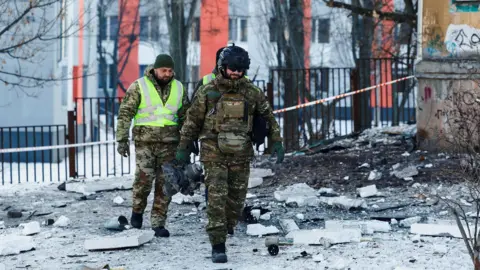 A police officer carries debris from a Russian drone near a cordoned residential building in snowy Kyiv, February 3, 2026.