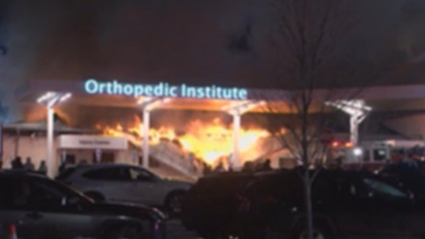 Thick smoke pours from the older orthopedic building attached to Lehigh Valley Hospital-Dickson City as firefighters work from aerial ladders at night.