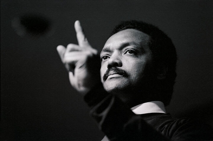 Portrait of Rev. Jesse Jackson with a raised hand.
