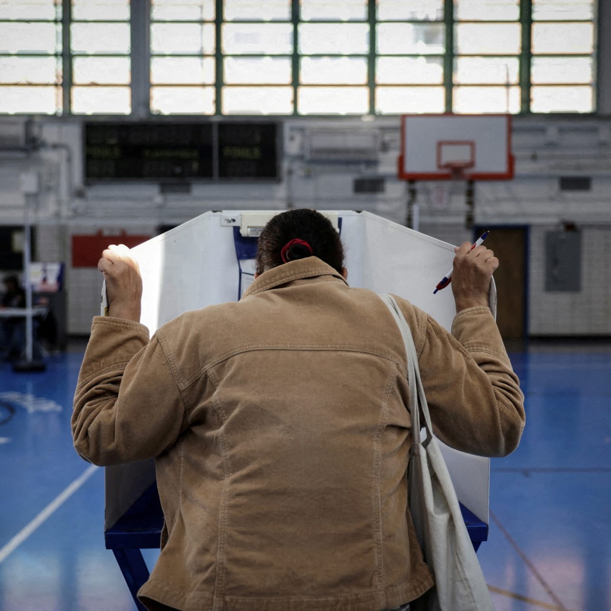 A woman holds the voting booth at an East Harlem school turned into a polling center on Election Day in Manhattan, New York, in 2024. Photo by Kent J. Edwards/Reuters - pbs