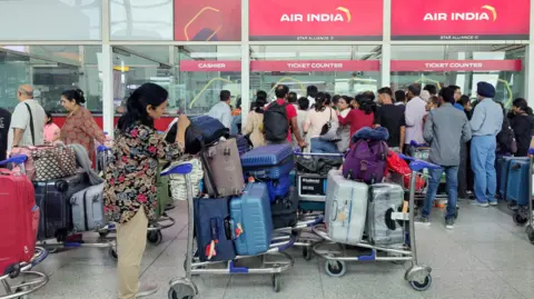 Passengers queue at Delhi airport amid delays and cancellations on rerouted flights.