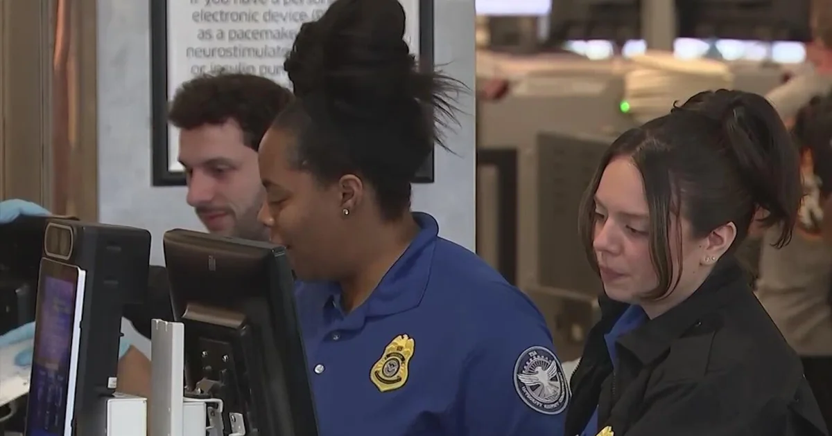 TSA officers work at an airport security checkpoint screening passengers