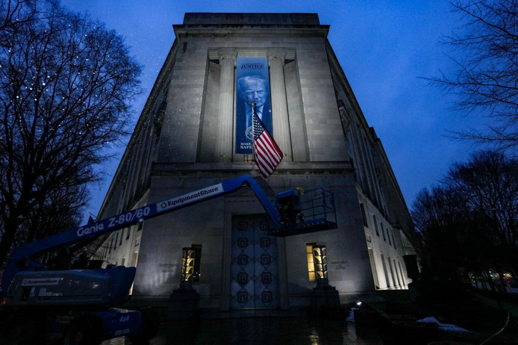 Workers install a banner depicting President Donald Trump on the Department of Justice building in Washington, D.C.